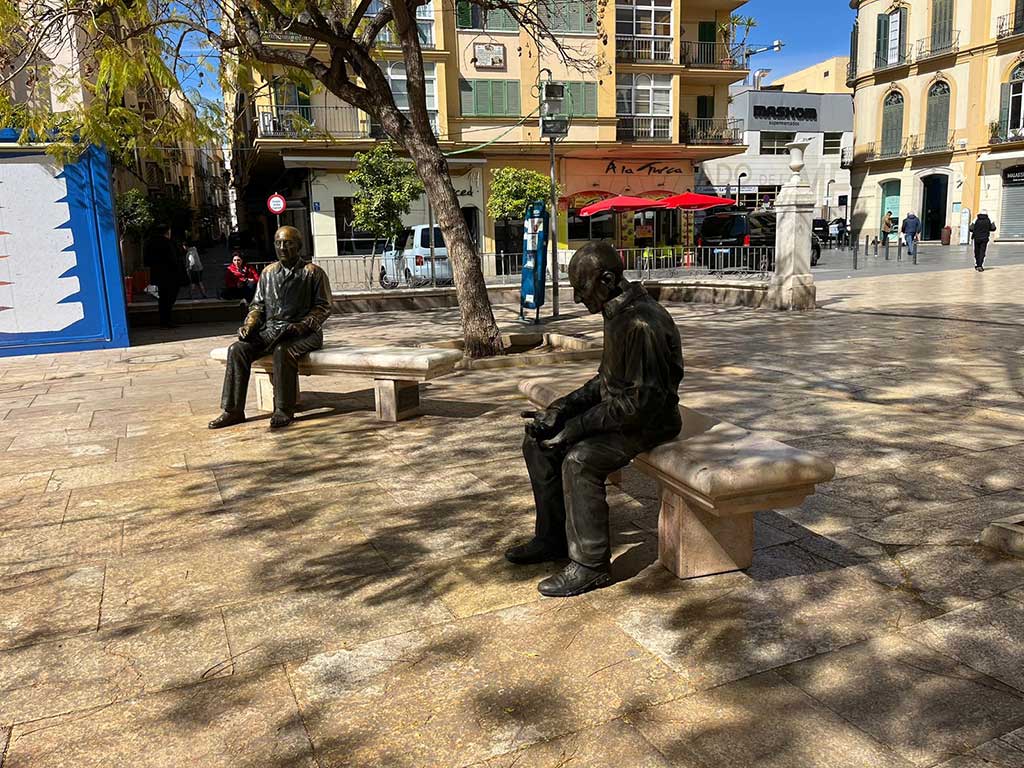 La figura de un anciano solo junto a la de Picasso llama la atención de paseantes en Málaga